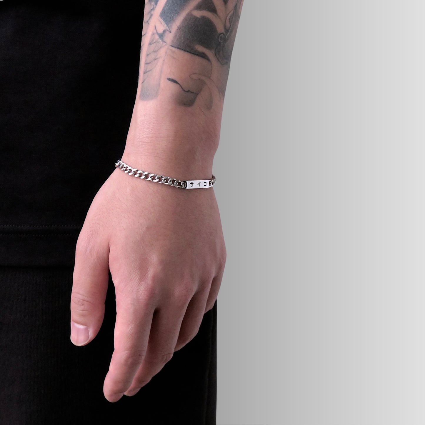 Male with tattooed arm wearing 316L stainless steel cuban chain bracelet with Japanese SAIKO logo