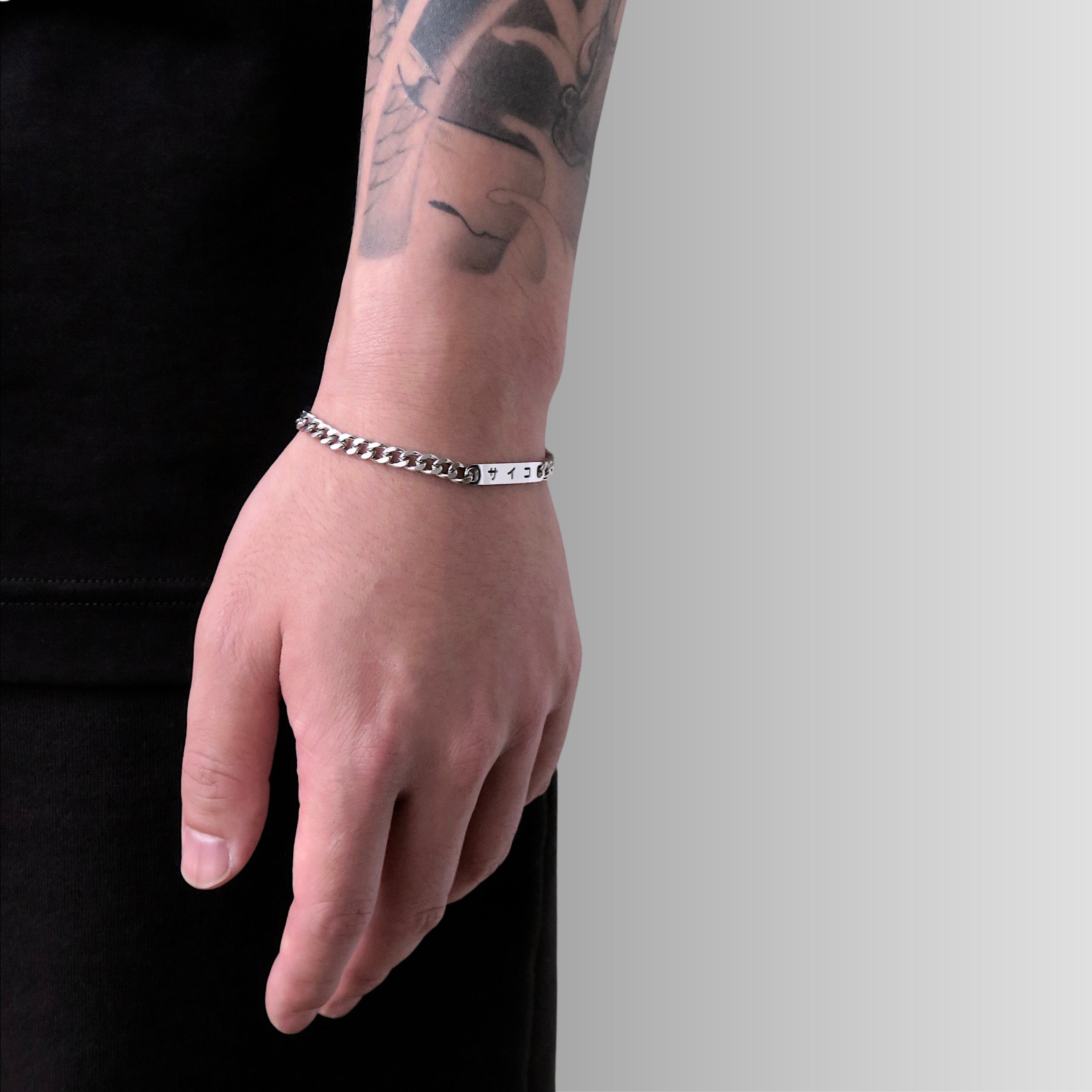 Male with tattooed arm wearing 316L stainless steel cuban chain bracelet with Japanese SAIKO logo