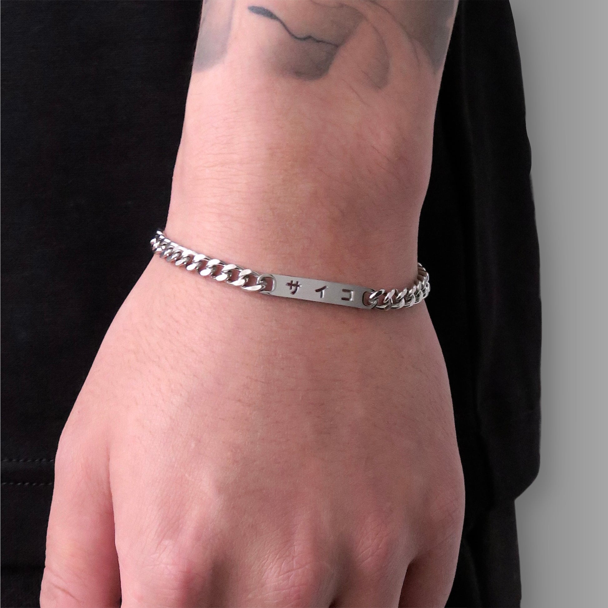 Close up of male with tattooed arm wearing 316L stainless steel cuban chain bracelet with Japanese SAIKO logo