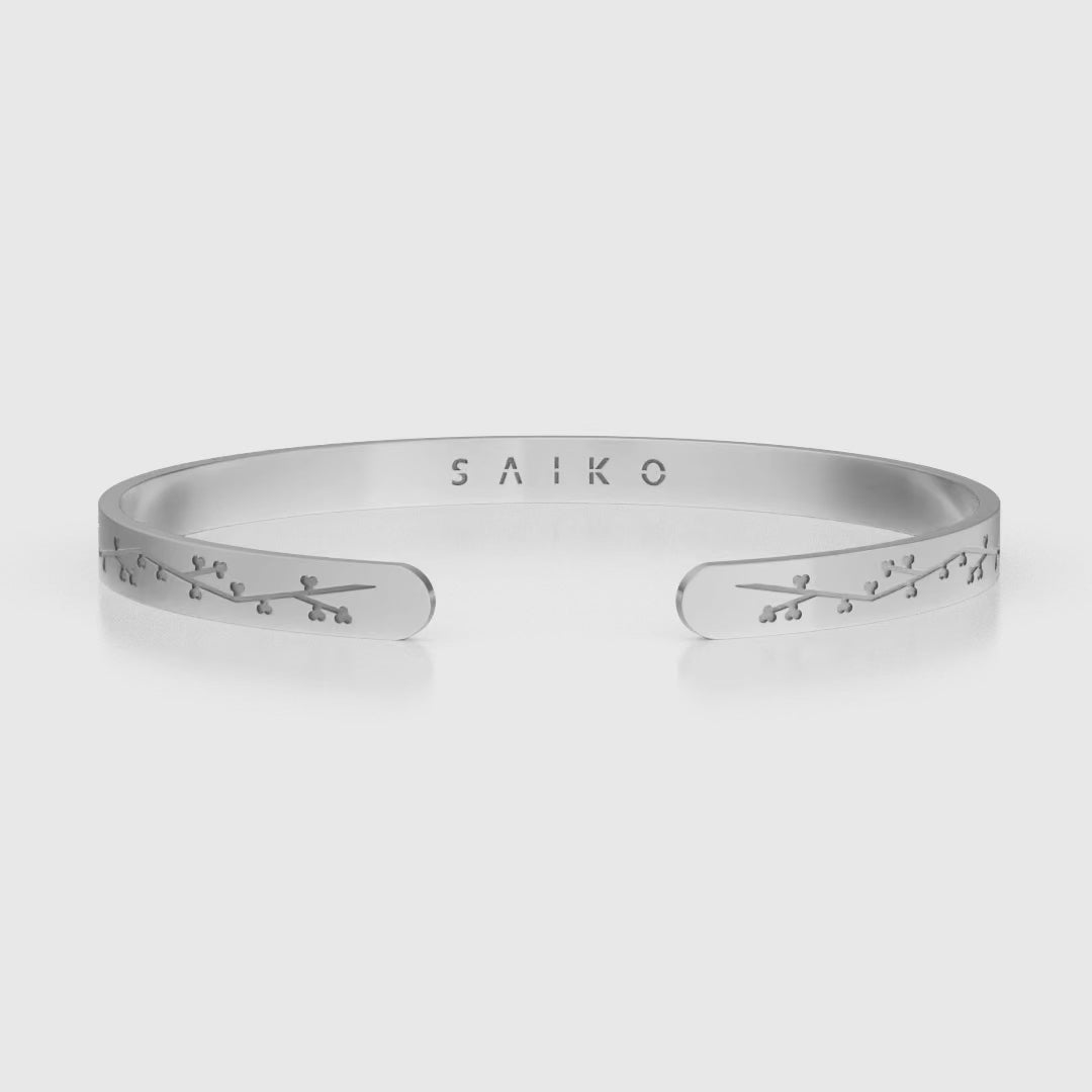 Silver stainless steel 316L cuff bracelet bangle with cherry blossom engraving placed on the ground rotating 360 degrees with a white background