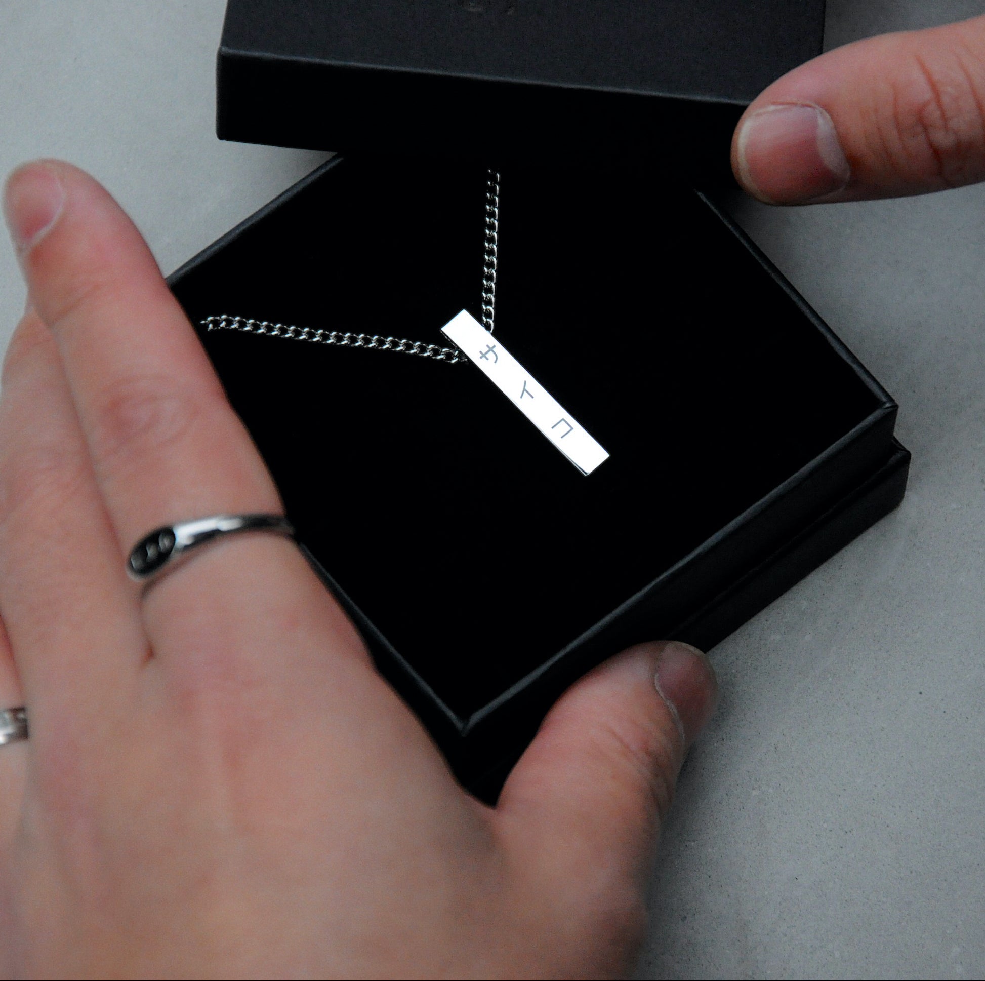 Unboxing a silver stainless steel 316L necklace with a vertical pendant and SAIKO logo form a black jewellery box