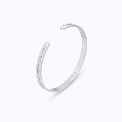 Silver stainless steel 316L cuff bracelet bangle with cherry blossom engraving placed on the ground with a white background